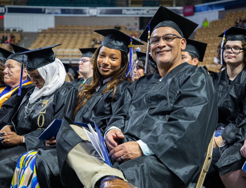 Two adult students smile in a row of graduates on commencement day