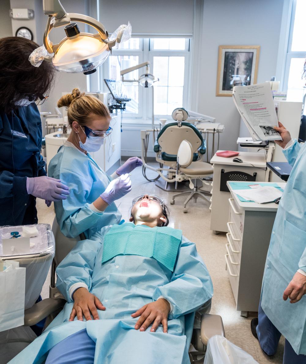 An instructor consults a document while two dental students work on a patient in the clinic