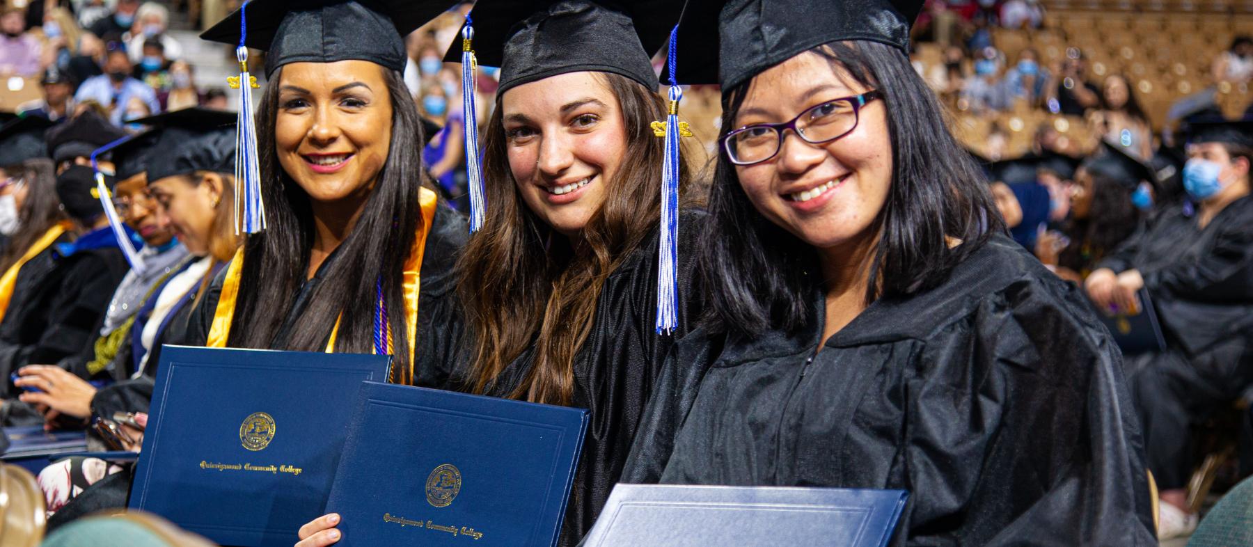 Three graduates in regalia show off their diplomas at commencement
