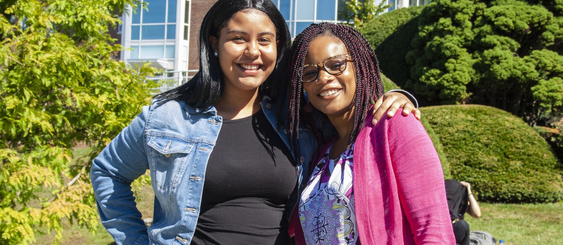 A mentor and mentee pair pose in front of the Harrington Learning Center on a summer day