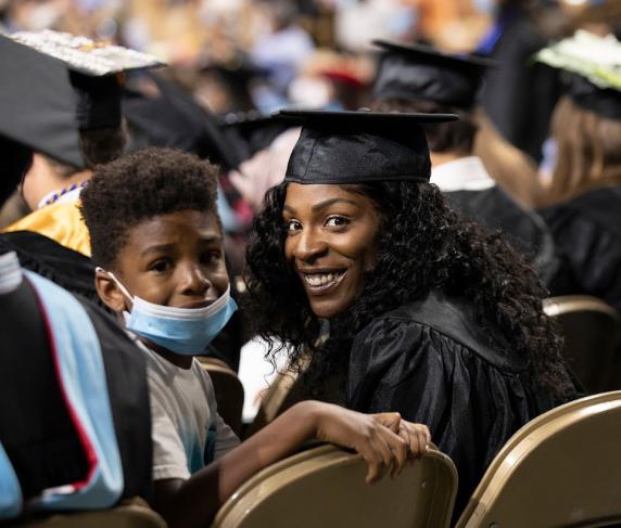A mother holding her son wait in the seats at commencement