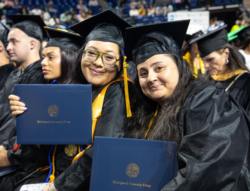 Two adult students smile in a row of graduates on commencement day
