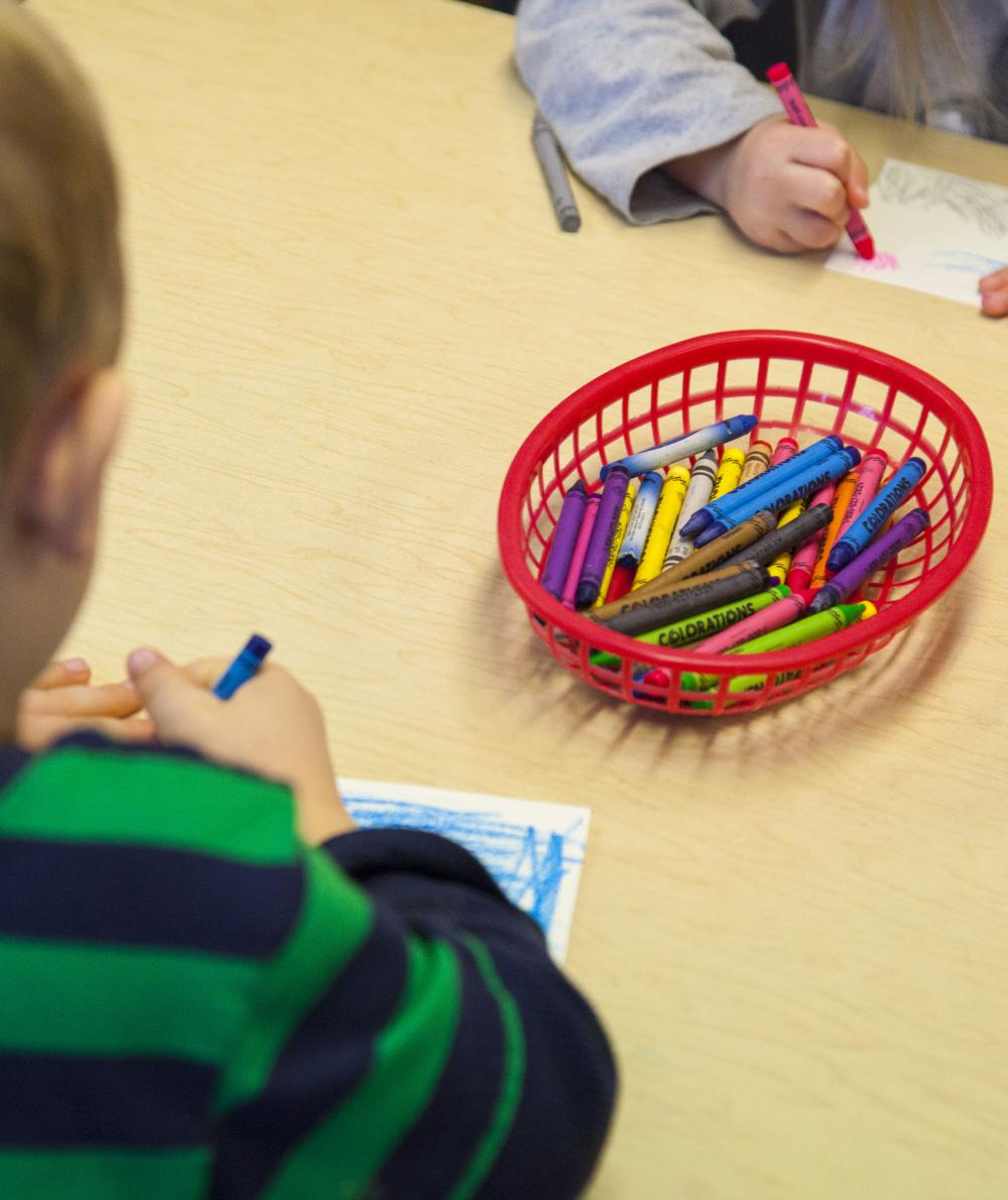 Young children sit at a desk and color