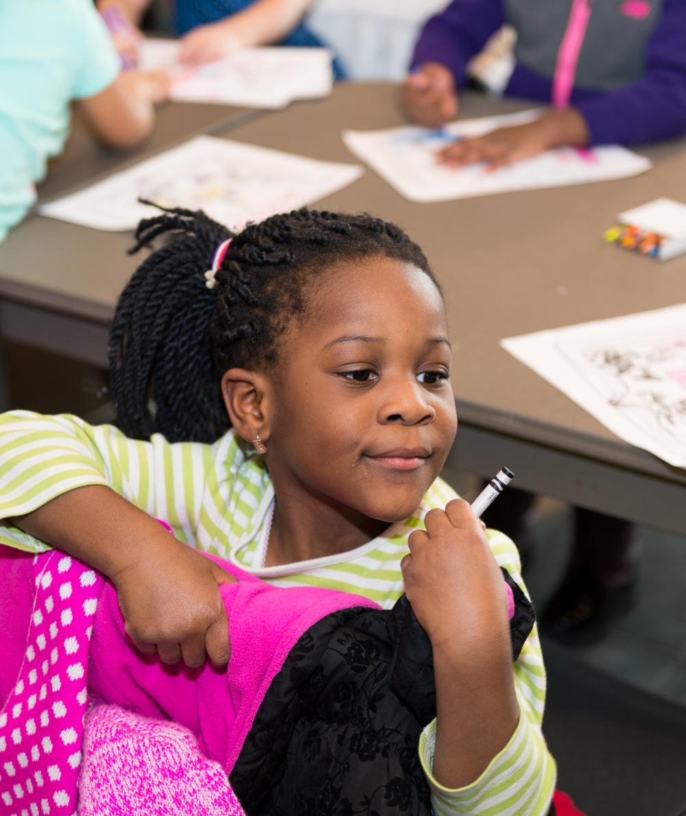 A young girl sits at a table where other children are drawing