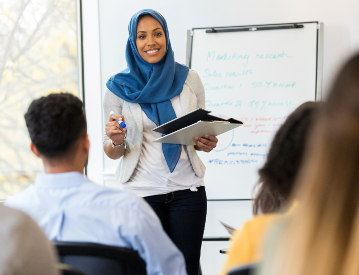 A woman stands in front of a whiteboard and teaches a class of new employees