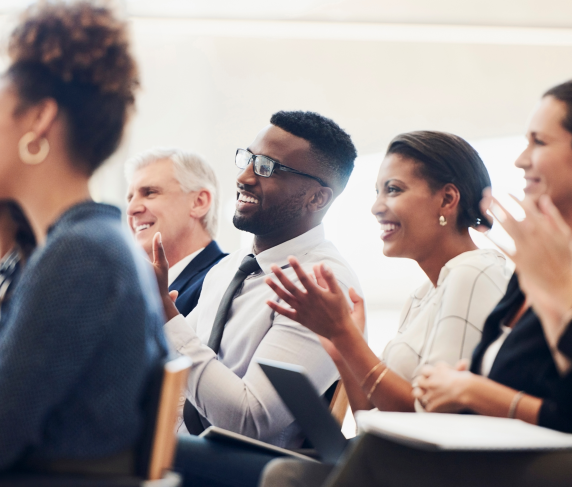 A group of professionals listen and clap in a lecture setting