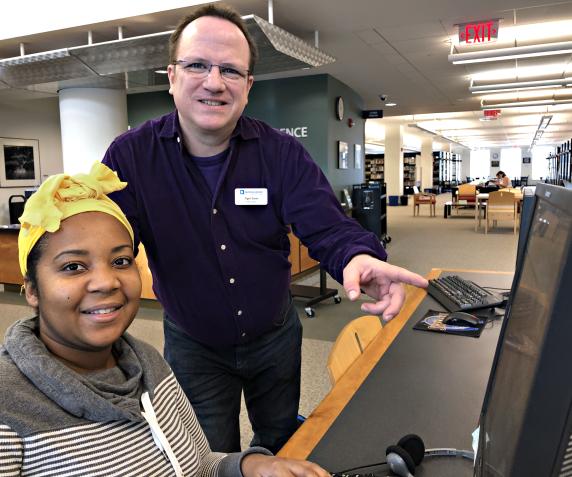 A staff member helps  a student on a computer in the library