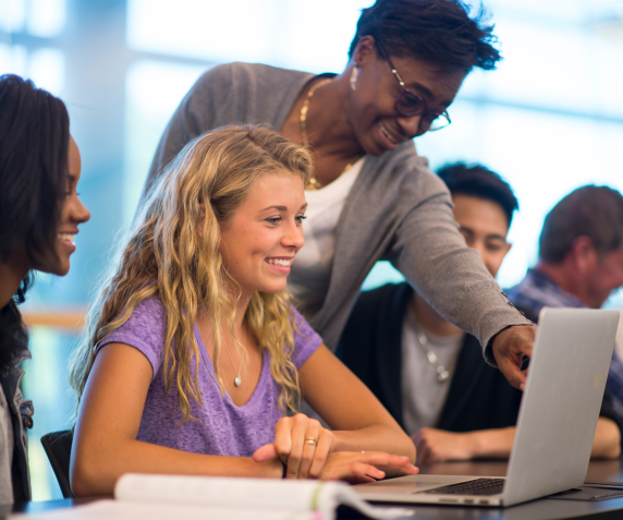 A staff member helps students register on a laptop in a classroom
