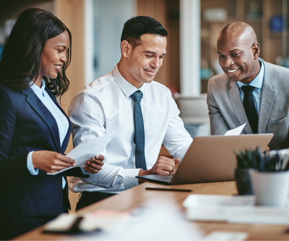 A group of three professionals discuss a document in an office setting