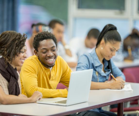 Students chat while following along with a lecture on their laptops in a classroom