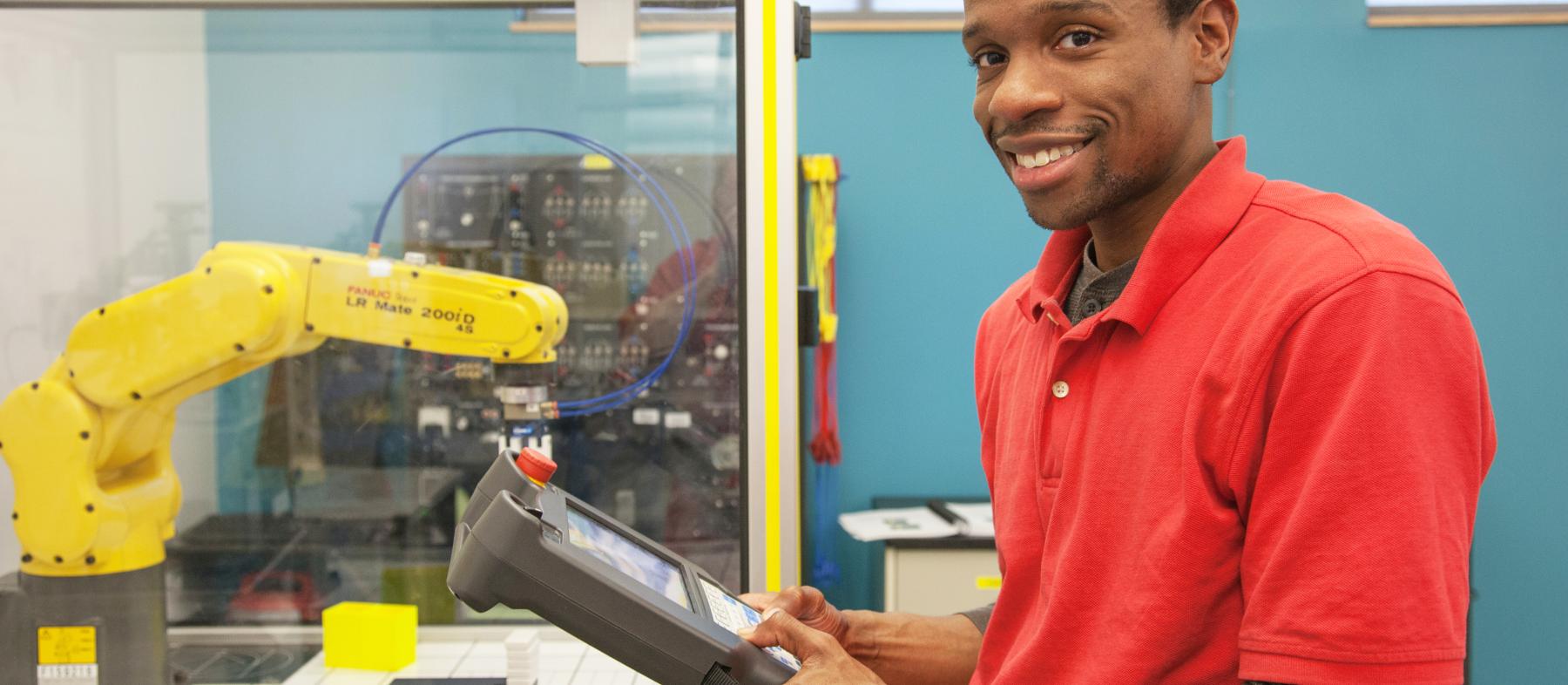 A student holds the controls to a robotic arm in an advanced manufacturing lab