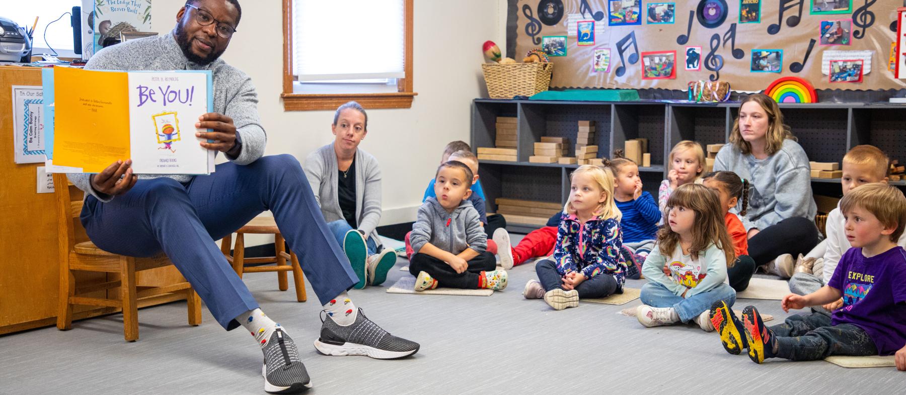 A staff member holds up a book for a class of young children