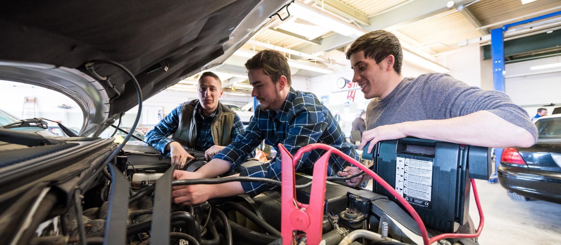 A professor oversees as two students work on a vehicle