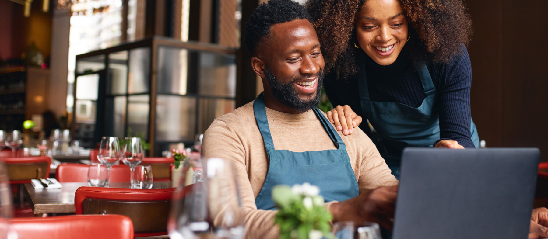 Two employees in a restaurant use a laptop