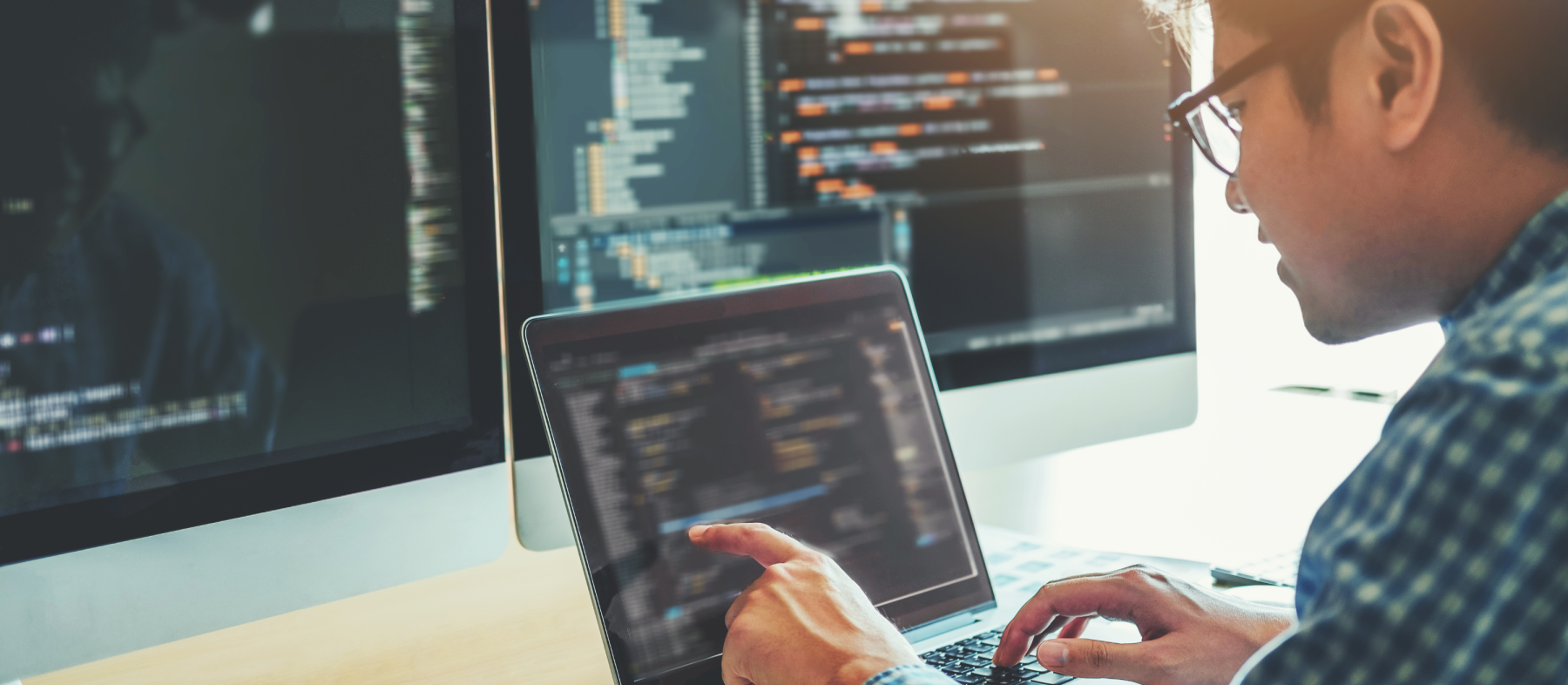 A man looks at code on multiple screens