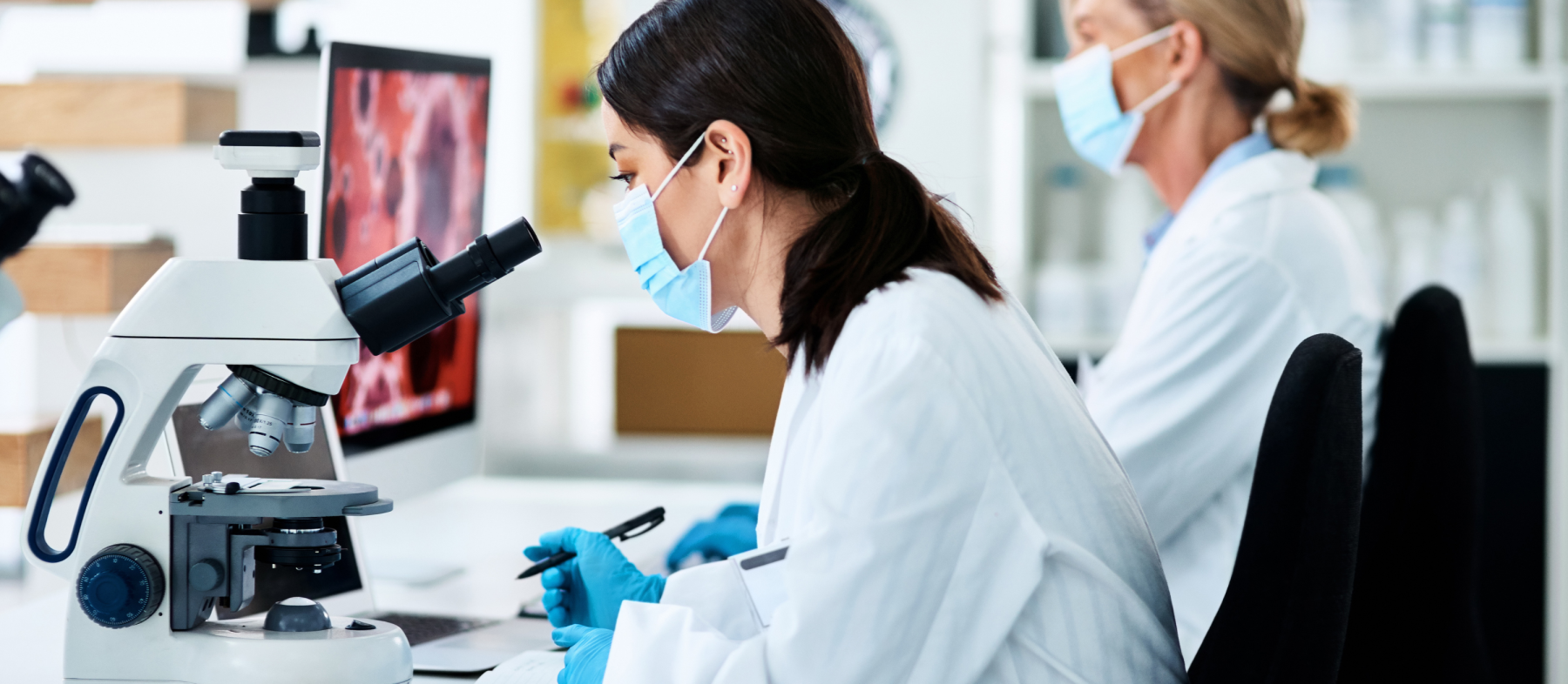 Two women work in a lab with a microscope