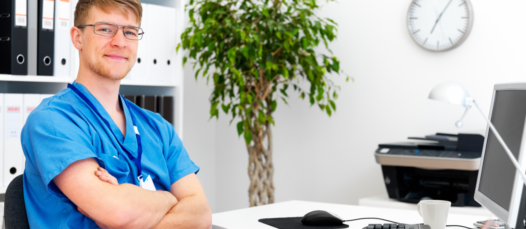 An employee in scrubs works at a desk in an office