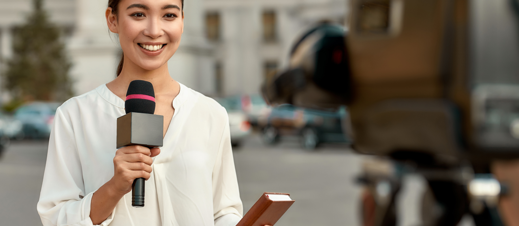 A reporter holds a mic and looks into camera on site