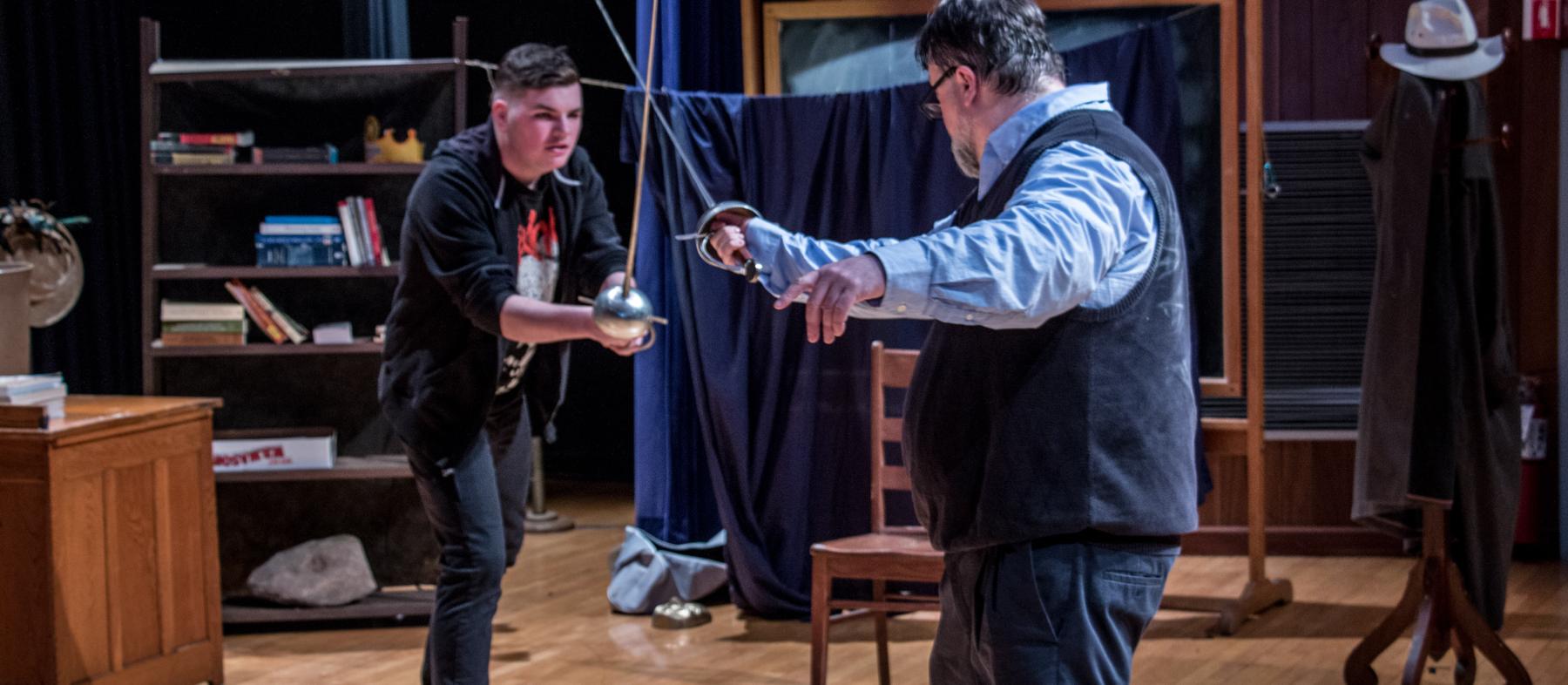 A professor and student playact a sword fight