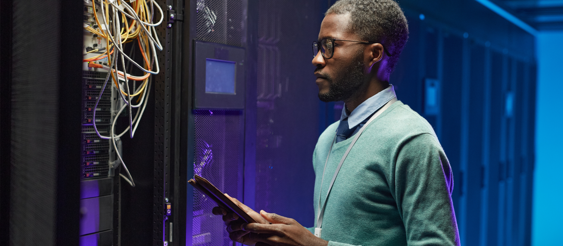 A man examines a bundle of wires in a mainframe room