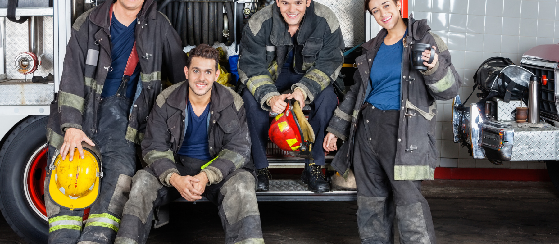 Four firefighters sit on the back of a fire truck.