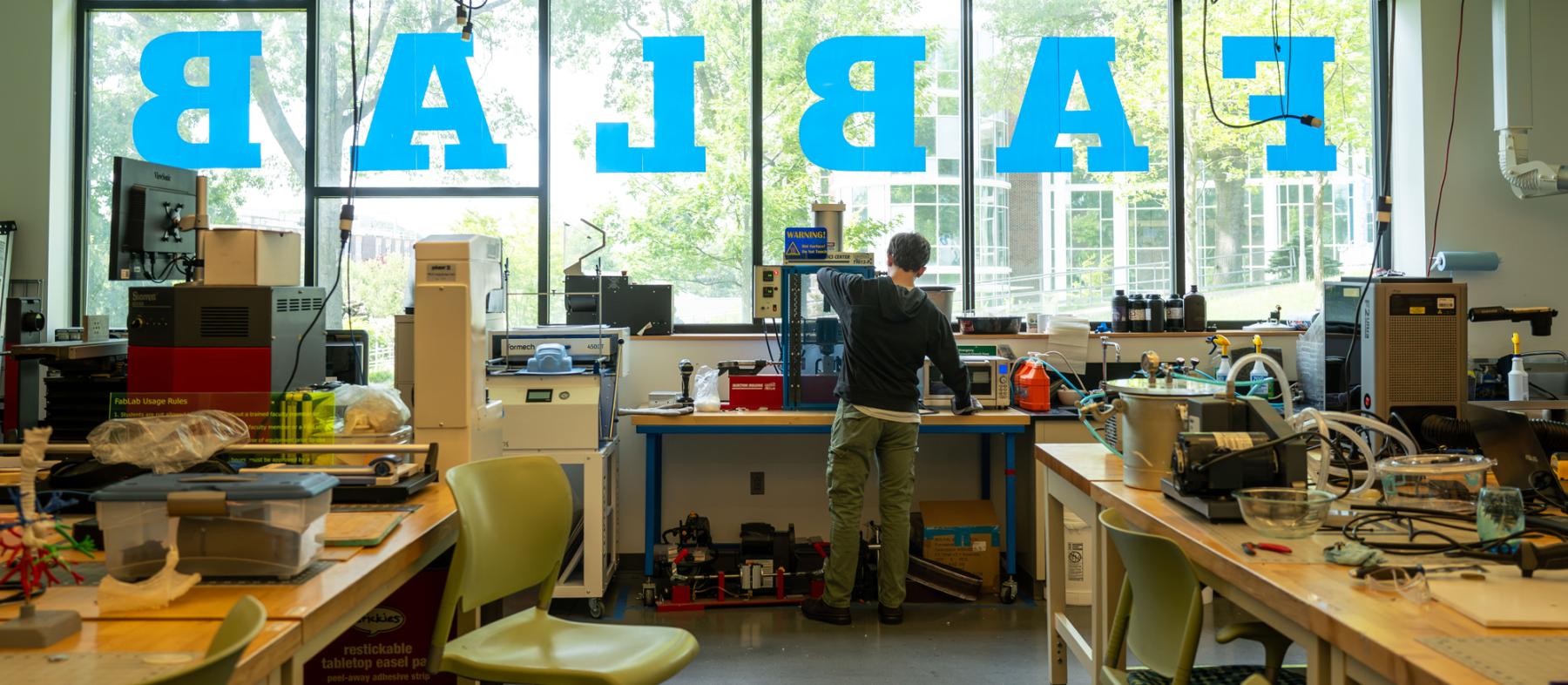 A wide shot of the fab lab with a male student working on one of the machines.