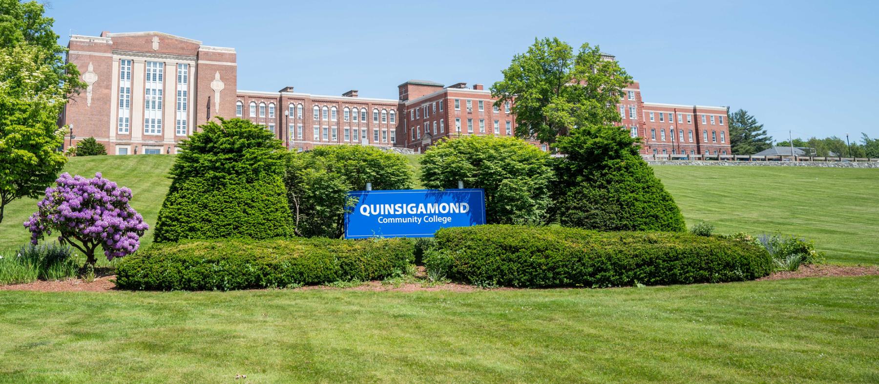 QCCs' front lawn with admin building a sign that says QCC