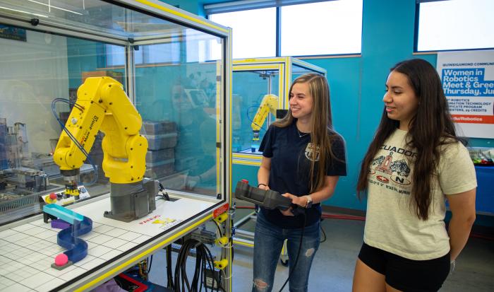 QCC graduate Anna Israelian (left) shows Jessica Calle how to use a FANUC robot. QCC graduate Anna Israelian (left) shows Jessica Calle how to use a FANUC robot.