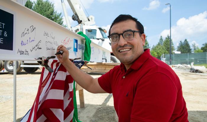 QCC alum Joshua Roman signs the ceremonial beam.