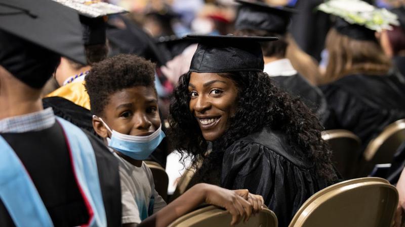 A mother holding her son wait in the seats at commencement