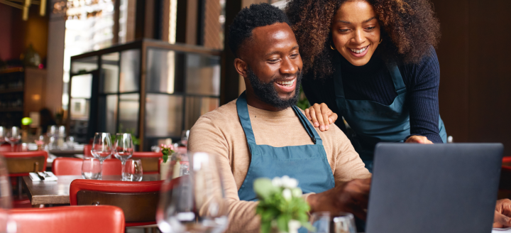 Two employees in a restaurant use a laptop