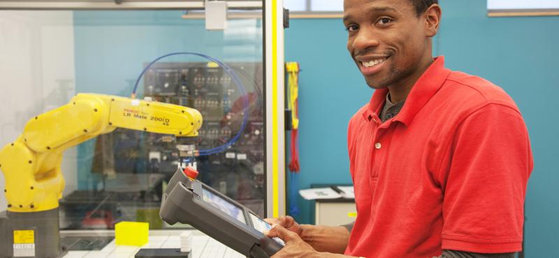 A student holds the controls to a robotic arm in an advanced manufacturing lab