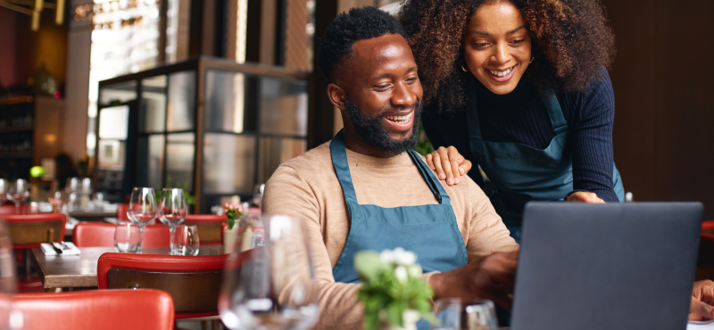 Two employees in a restaurant use a laptop