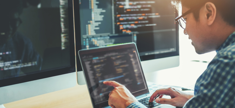 A man looks at code on multiple screens