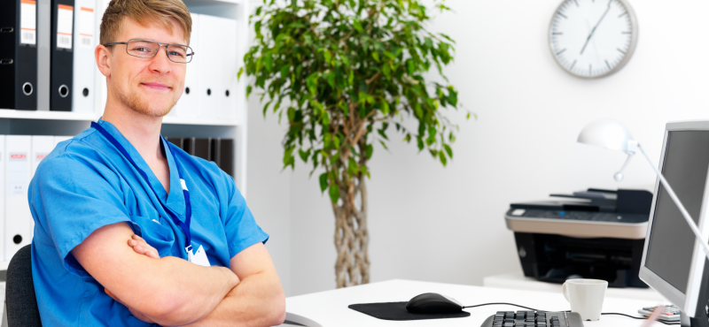 An employee in scrubs works at a desk in an office