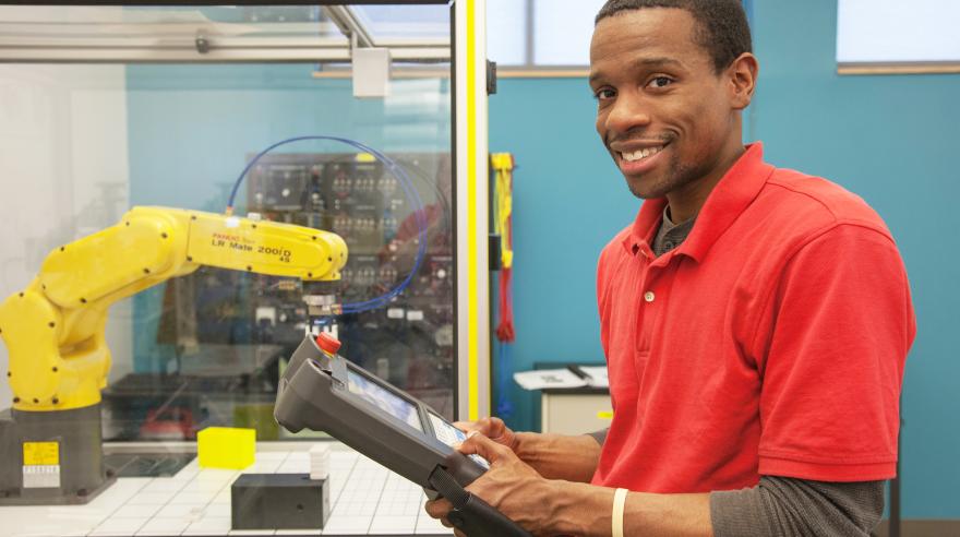 A student holds the controls to a robotic arm in an advanced manufacturing lab